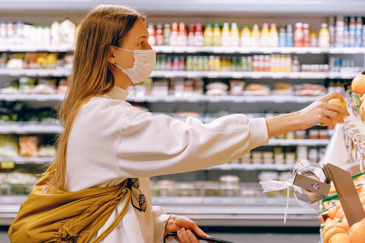 Woman wearing a face mask while selecting fruit in a supermarket, highlighting safety measures.