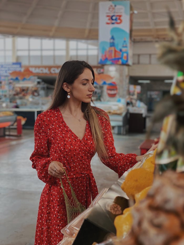 A stylish woman in a red dress shops for produce in an indoor market setting.